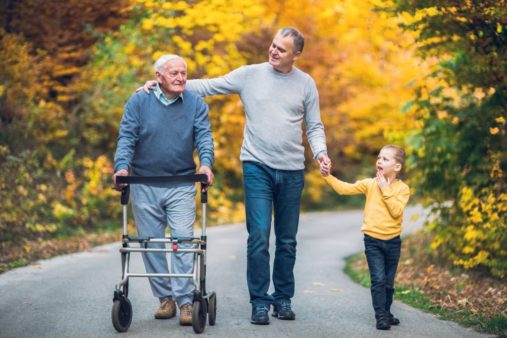 An elderly father with a walker, adult son and grandson out for a walk in the park